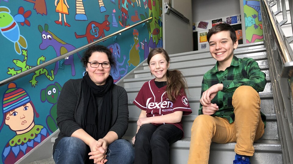 Ariane Ouellet, Félix et Guillaume sont assis dans les escaliers qui longent le mur de la murale.