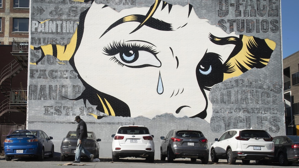 Un passant devant une murale illustrant une femme qui pleure.