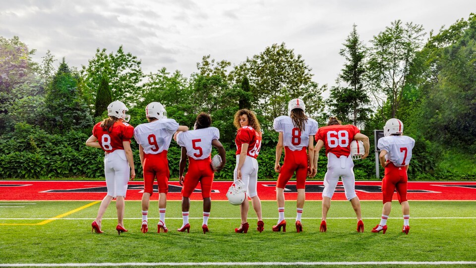 Sept joueurs et joueuses de football posent dos à la caméra sur un terrain de football.