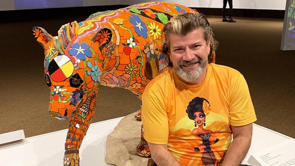 L'artiste Michel Dumont assis devant son œuvre, un ours en mosaïque.