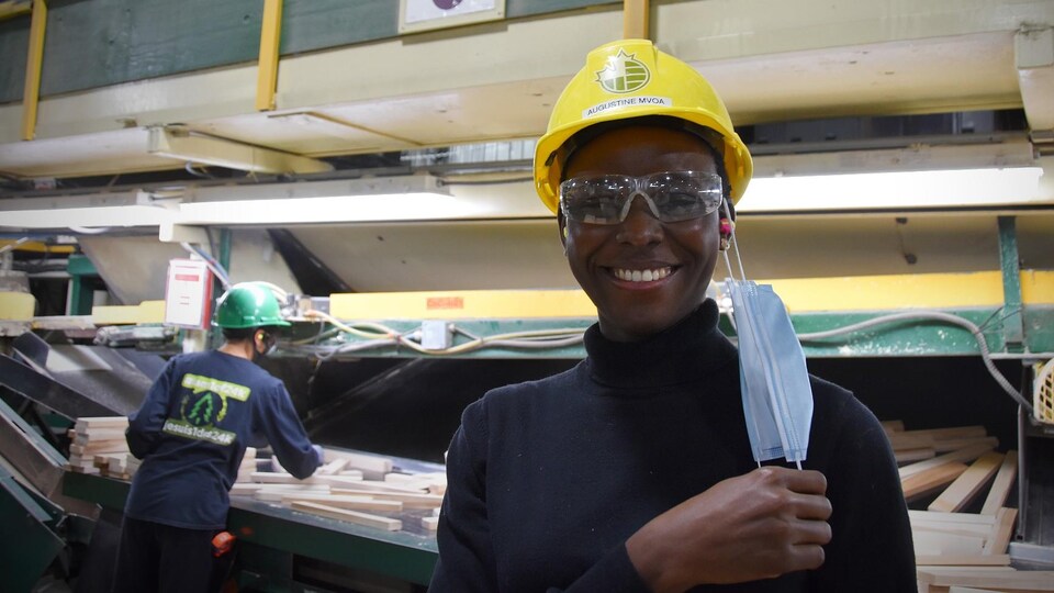 Augustine Mvoa-Ambomo, souriante, devant une machine d'où sortent des pièces de bois.