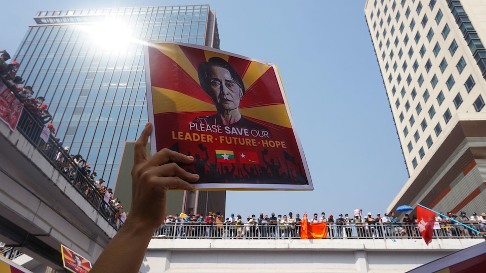 Une main brandie une affiche d'Aung San Suu Kyi. On peut y lire : « SVP, sauvez notre leader, notre futur, notre espoir ».
