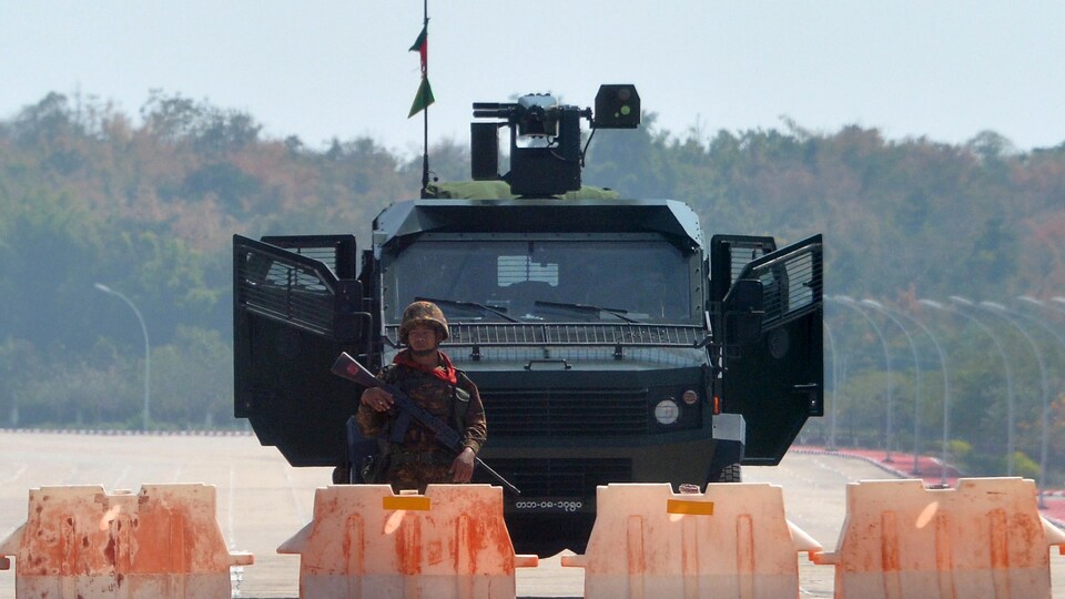 Un soldat armé devant un véhicule blindé.