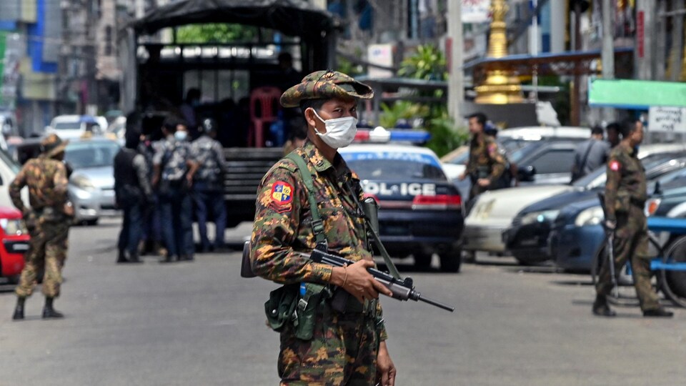 Un soldat birman porte une arme automatique, et scrute les alentours dans une rue achalandée.