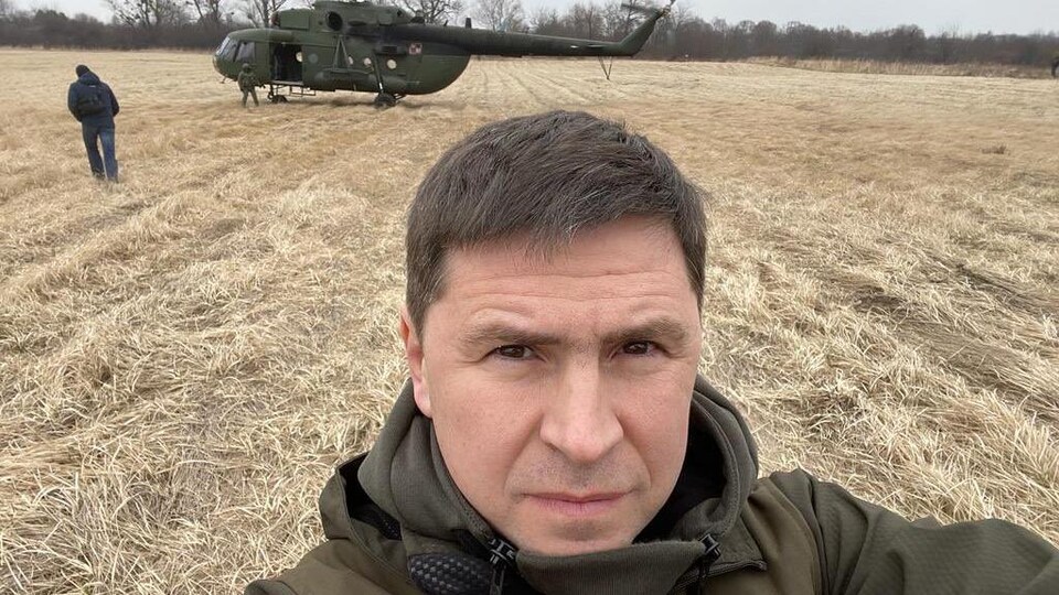 Autoportrait de Mykhaïlo Podoliak, dans un champ, près d'un hélicoptère.