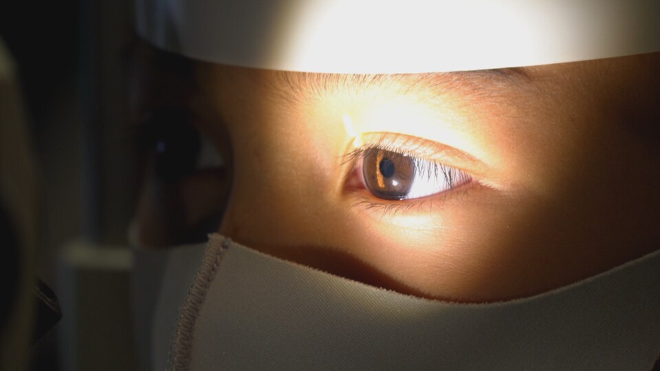 Gros plan sur le visage d'un enfant qui passe un examen de la vue. Une lumière éclaire l'un de ses yeux. Il porte un masque 