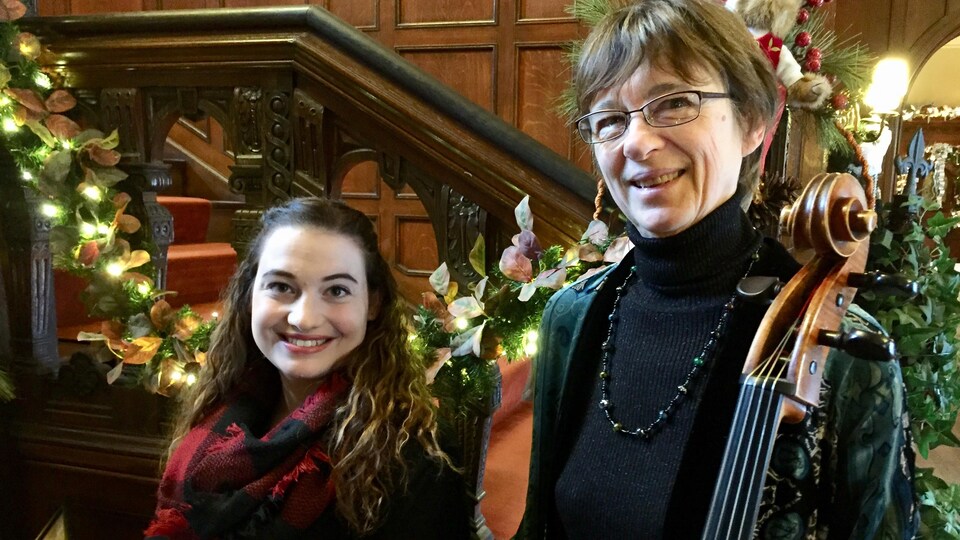 2 femmes souriantes sont debout à côté d'un escalier qui est tout décoré pour le temps des fêtes