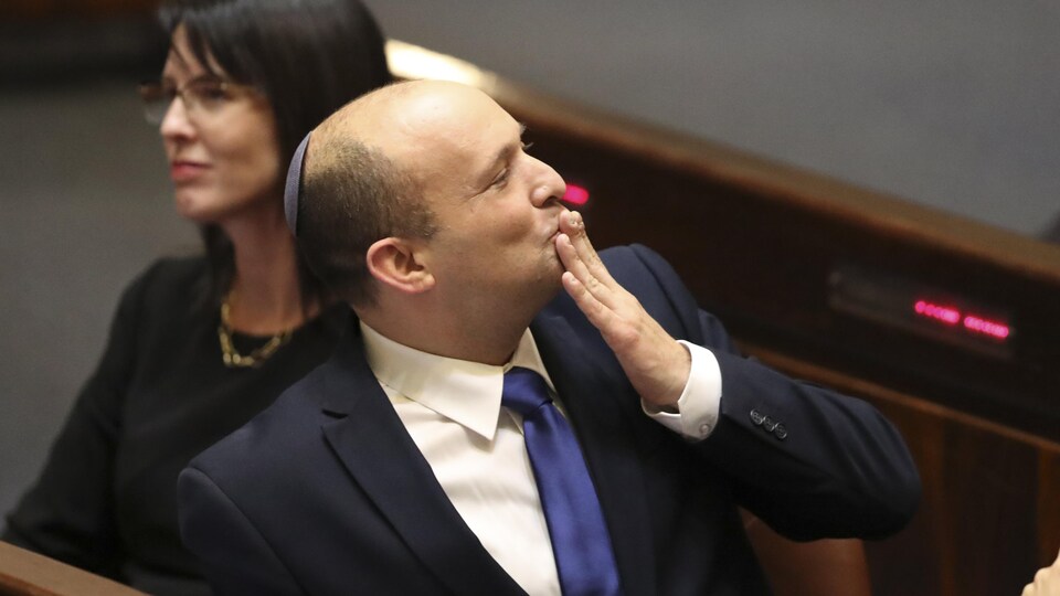 Naftali Bennett assis au parlement, la main portée aux lèvres.