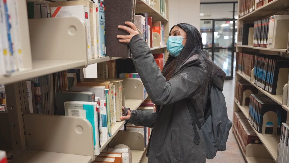 Najwa dans la bibliothèque du Cégep de Sherbrooke. Elle regarde des livres dans un rayon. 