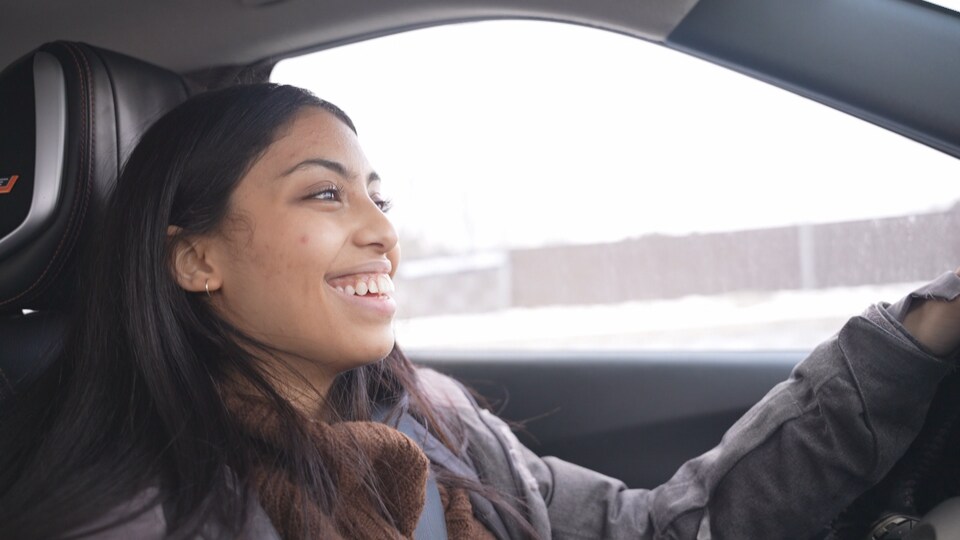 Najwa Badawi au volant de sa voiture. Elle sourit à pleines dents. 
