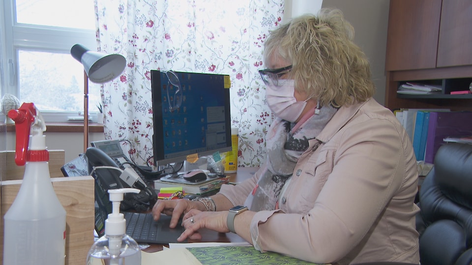 Une femme porte le masque et écrit sur son ordinateur portable.