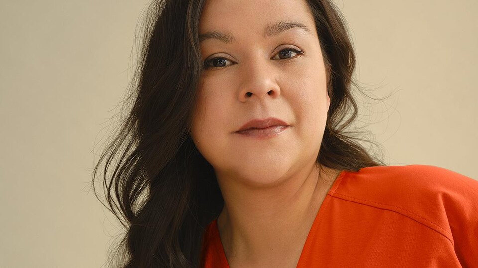 Naomi Fontaine sourit. Elle porte un gilet orange.