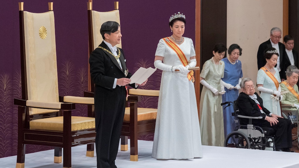 Un homme, accompagné d'une femme sur un podium, lit un texte.