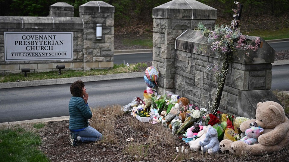 Une femme se recueille devant des fleurs et des peluches.