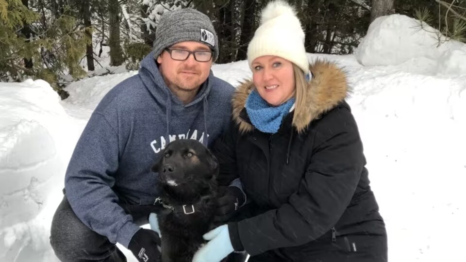 Natalie Lachance et Chris Byerley accroupis dans la neige avec un chien noir
