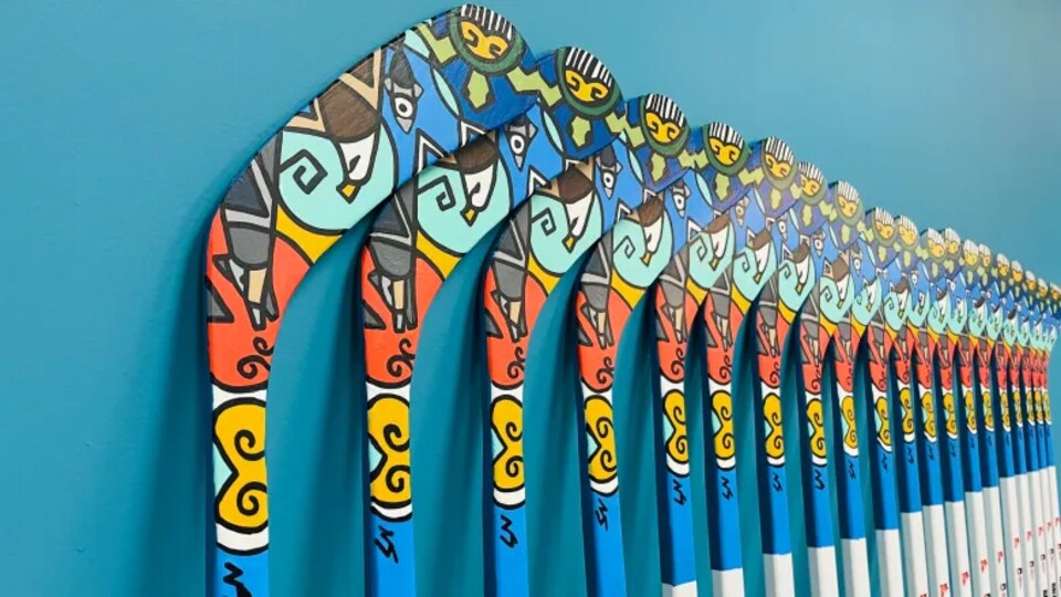 20 bâtons de hockey placés contre un mur bleu. 