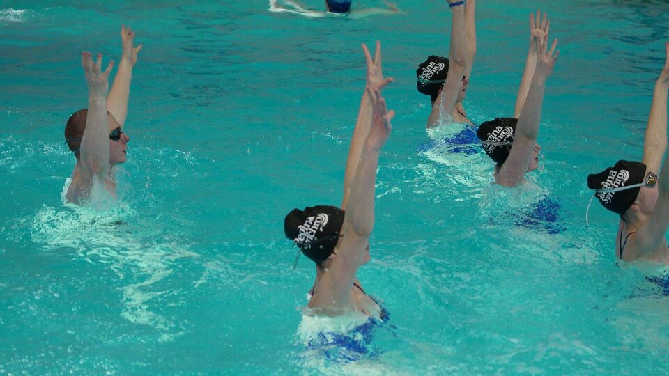 Un homme dans une piscine fait de la natation artistique avec des coéquipières.