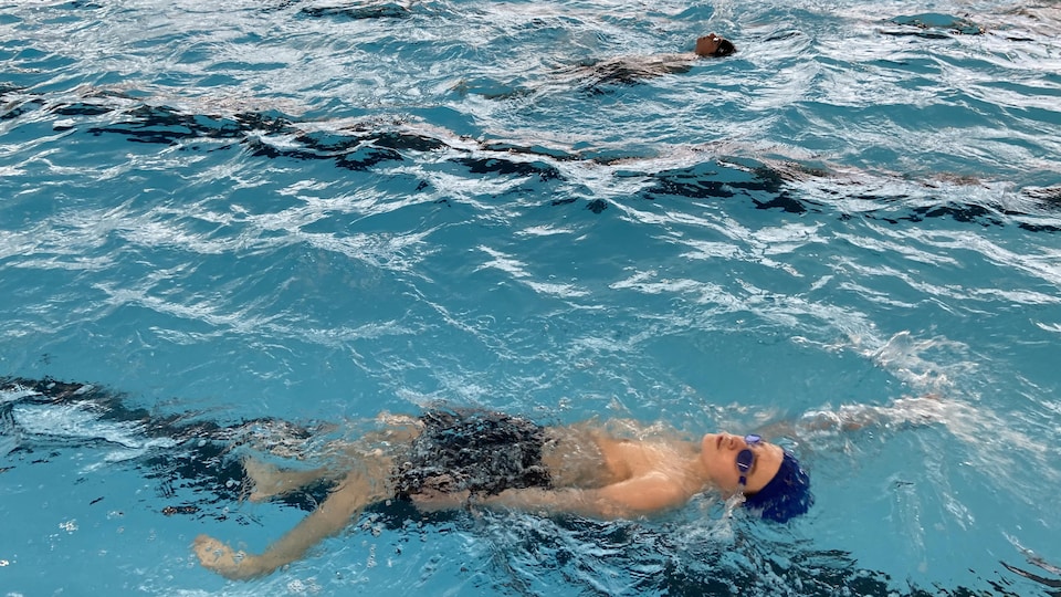 Des adolescents nagent sur le dos dans une piscine intérieure.