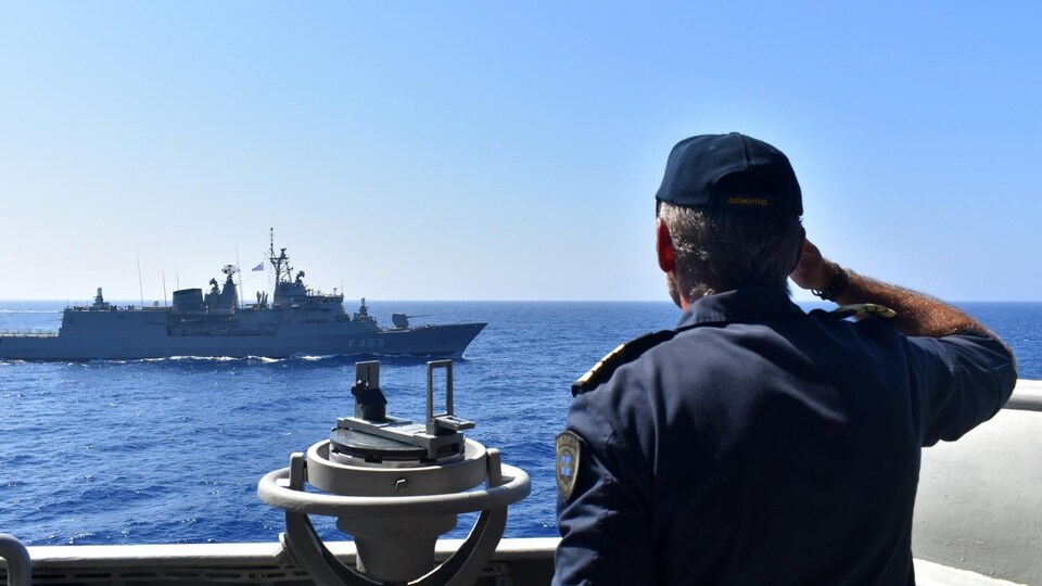 Un marin regarde un bateau de guerre au loin.