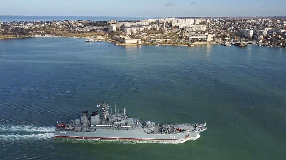 Un navire de guerre avance sur l'eau près d'une grande ville.