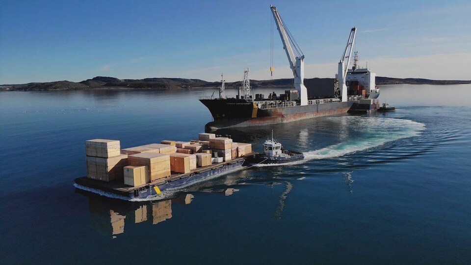 Un navire de ravitaillement de l'entreprise Desgagnés Transarctik décharge des caisses de bois sur une barge.