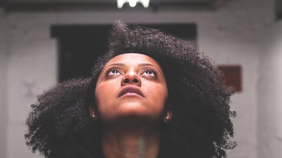 Portrait de la rappeuse Naya Ali, qui regarde vers un néon au plafond.