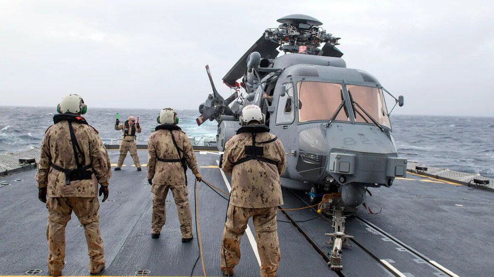 Une équipe militaire entoure un hélicoptère sur le pont du navire.