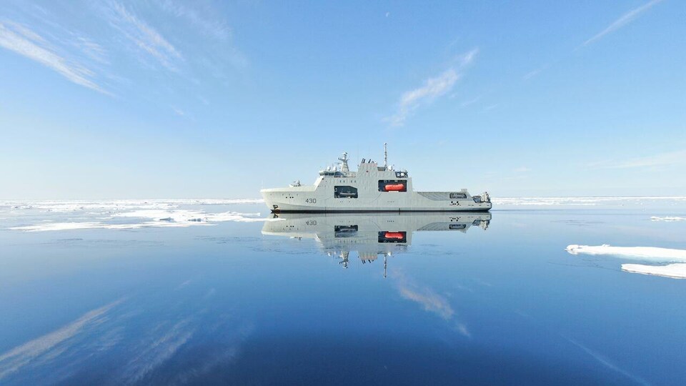 Le NCSM Harry DeWolf navigant sur un océan où flottent quelques plaques de glace.