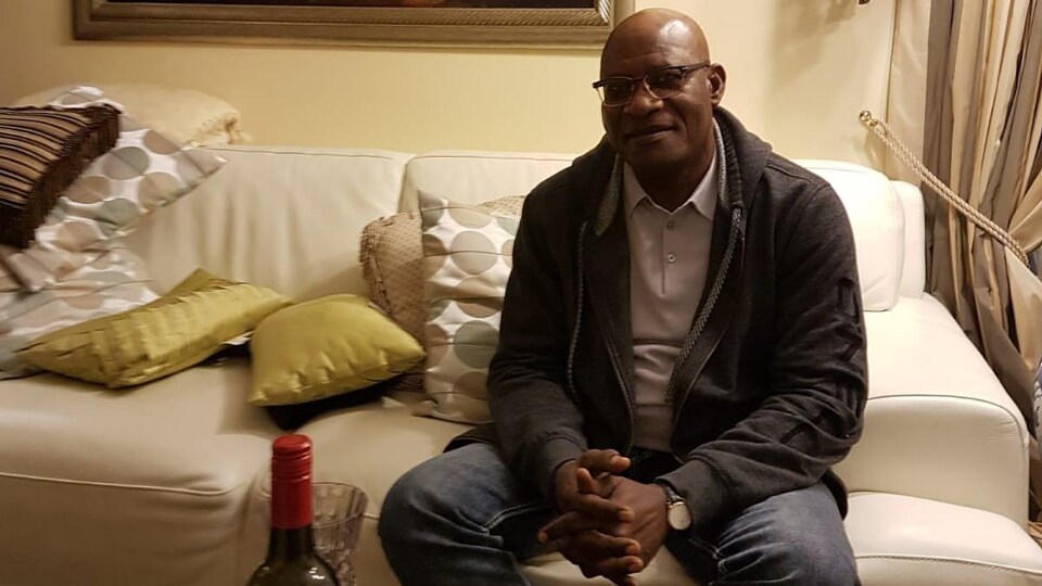 Un homme assis sur un sofa, dans un salon.