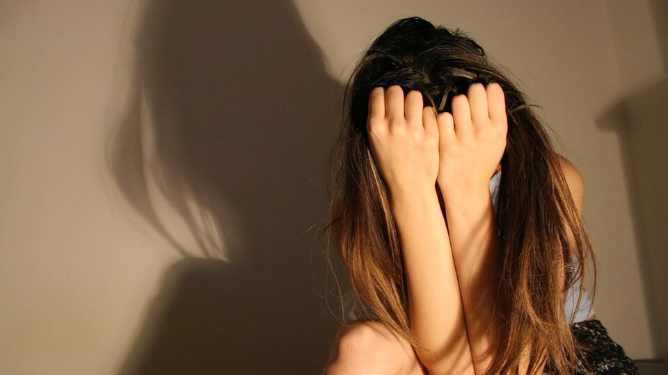 Une jeune femme vit une grande détresse, dans une pièce peu éclairée.
