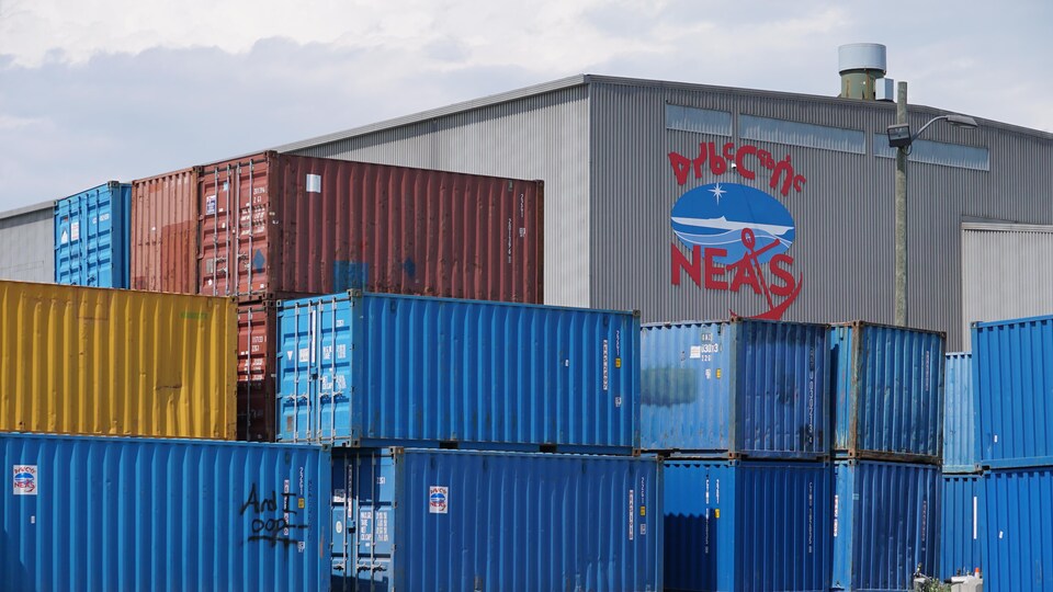 Le logo de NEAS sur une bâtisse et des conteneurs empilés l'un sur l'autre devant.