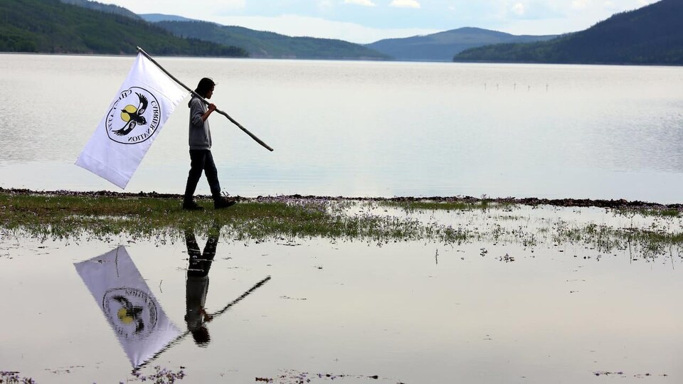 Un homme porte un drapeau en marchant le long de l'eau.