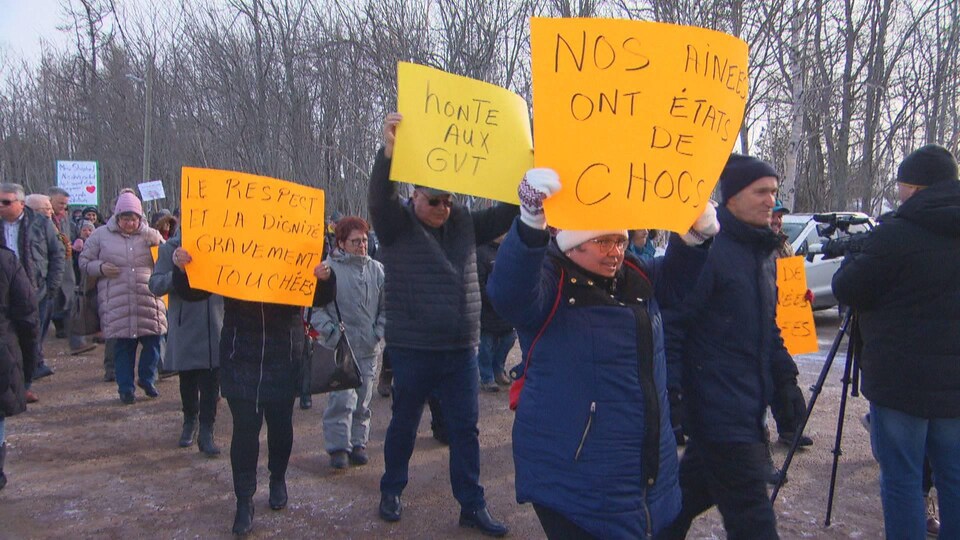 Des dizaines de personnes marchent dans la rue en hiver. Sur leurs pancartes, on lit des messages tels : « Honte aux gouvernements », « Nos ainees ont états de chocs » et « Le respect et la dignité gravement touchées ».
