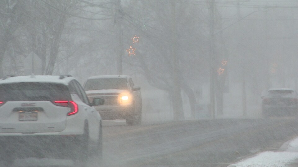 Des voitures se déplacent sur une route de Caraquet, la visibilité n’est pas très bonne en raison de chute de neige. 