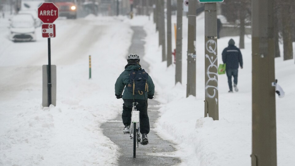 Une rue enneigée de Montréal où l'on voit notamment un cycliste de dos sur une piste cyclable.