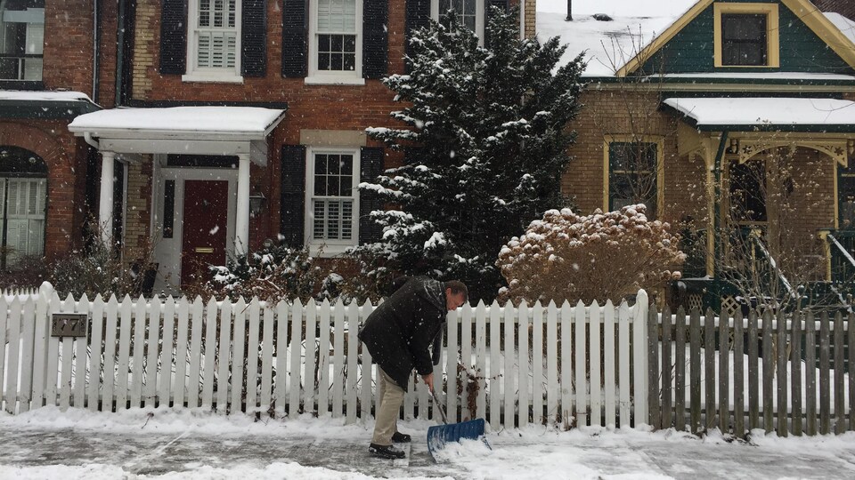 Un homme déblaie la neige sur le trottoir devant sa résidence, dans le quartier Cabbagetown à Toronto. 