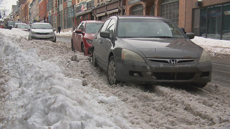 Trois voitures obstruent une partie de la rue puisqu'elles ne peuvent pas se garer près des trottoirs en raison de la neige. 