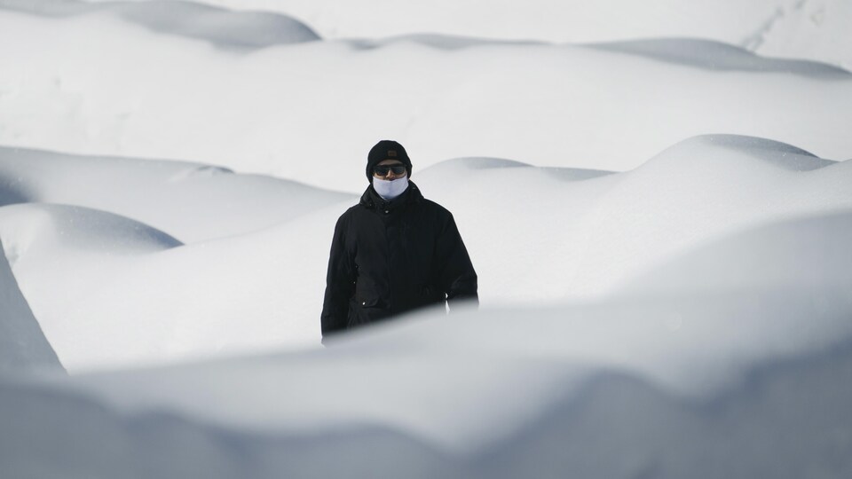 Un homme masqué marche dans des dunes de neige.