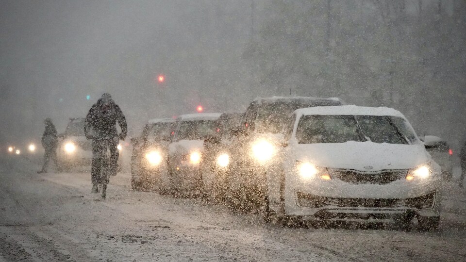  Des voitures et un cycliste se déplacent sous la neige.                              