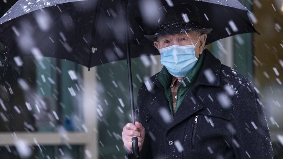 Un homme marche sous la neige avec un parapluie. Il porte un couvre-visage.