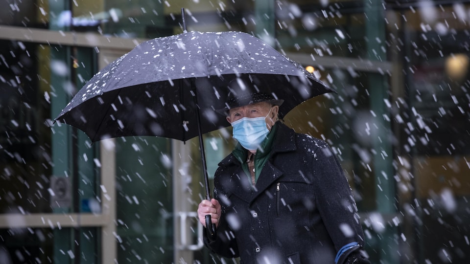 Un homme marche sous un parapluie alors qu'il neige à Surrey, dans le Grand Vancouver.