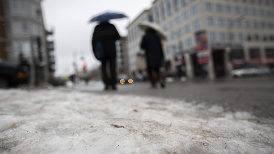 Deux personnes marchant sur la rue, protégées des averses par un parapluie.