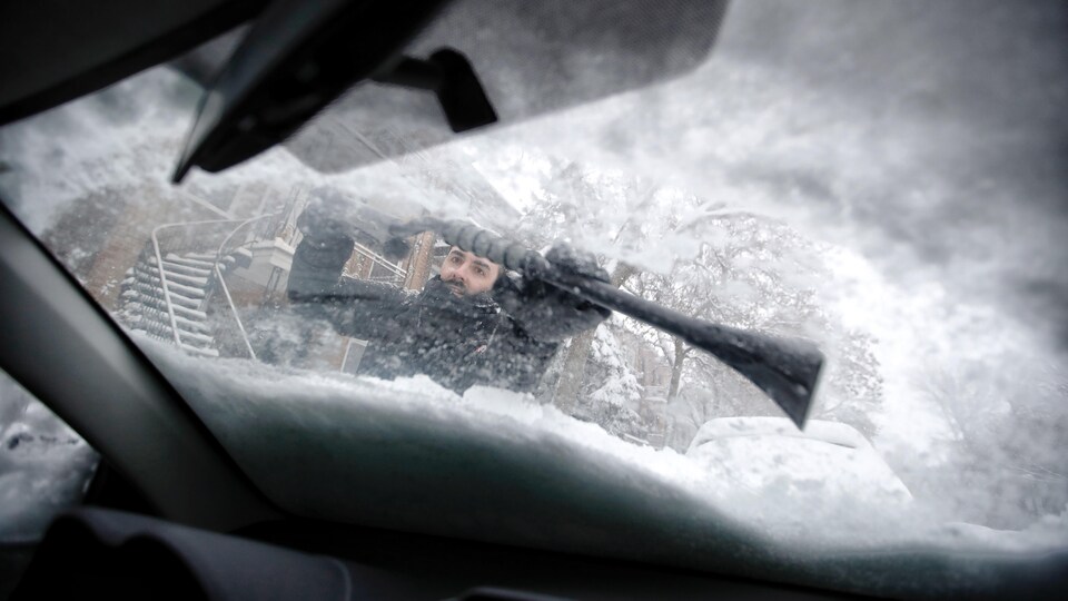 Un homme déneige sa voiture.