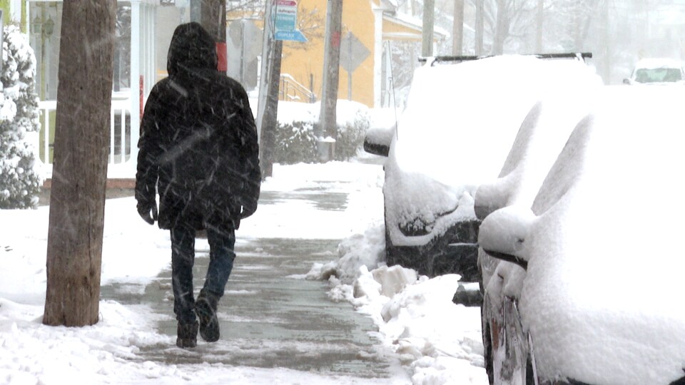 Une personne marche sur un trottoir semi-enneigé.