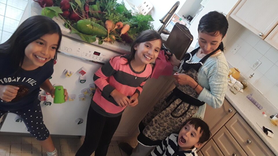 Nelcy Lopez et ses trois enfants s'amusent dans leur cuisine. Des fruits et légumes sont posés sur le comptoir.