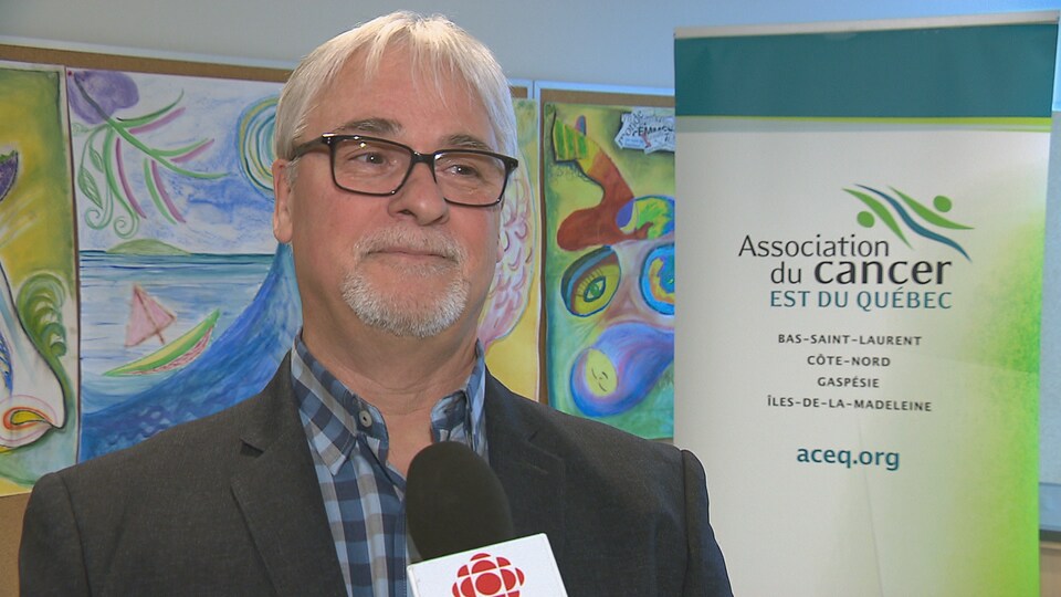 Le directeur général de l'Association du cancer de l'Est du Québec, Nelson Charette, en plan rapproché. Derrière lui se trouve une pancarte qui affiche «Association du cancer de l'Est du Québec».