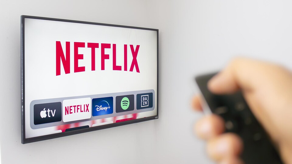 Une personne tient d'une main une télécommande utilisant l’application Netflix.