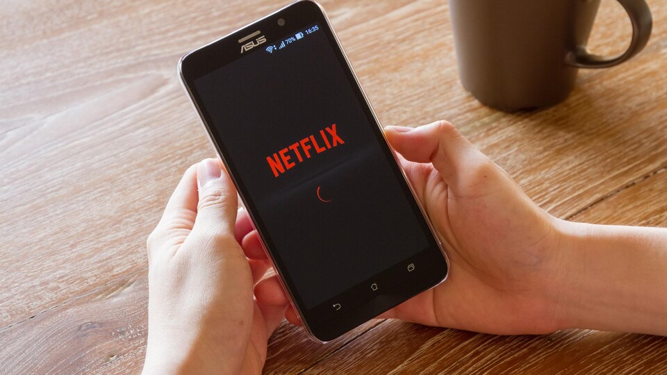 Un homme tient un téléphone intelligent sur lequel apparaît le logo de Netflix.