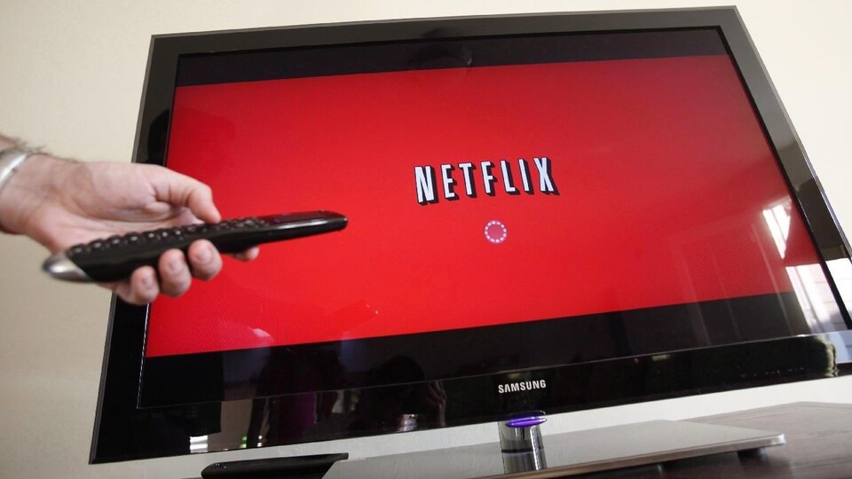 Une main tient une télécommande pointée vers une télévision affichant le logo de Netflix.