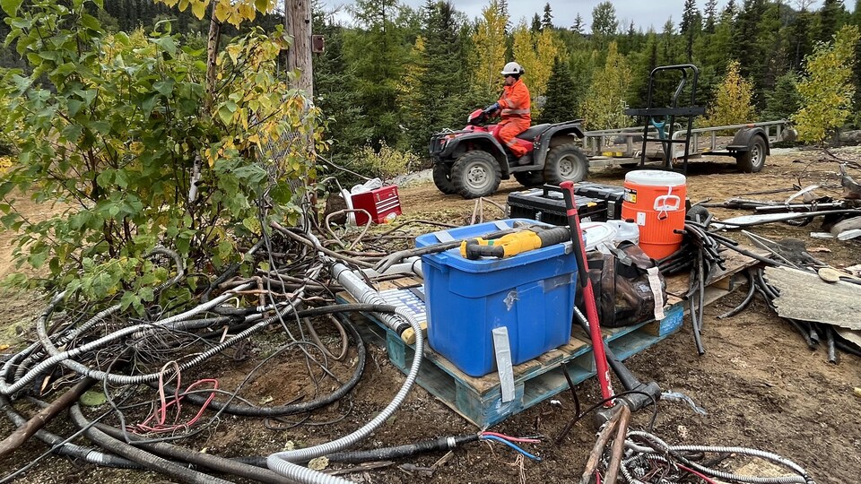 Un homme en véhicule tout-terrain traîne une remorque au milieu de deux piles de débris, dans la nature.
